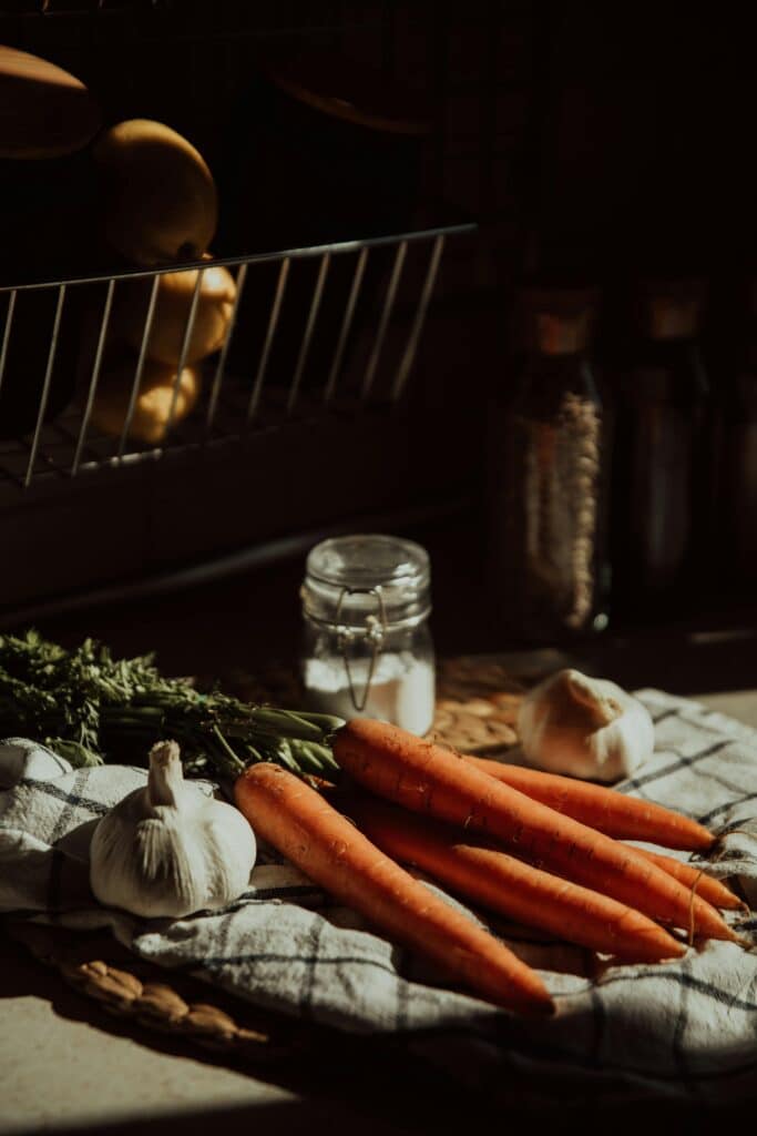 pexels-photo-6065707-6065707 Moody kitchen composition featuring fresh carrots, garlic, and spices on a cloth.